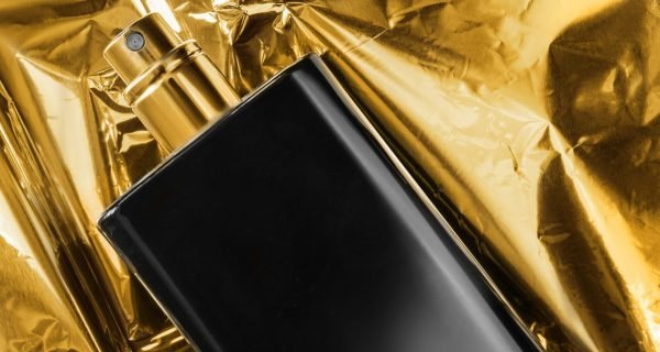 Perfume on foil background Black glass perfume spray bottle lying on golden foil background